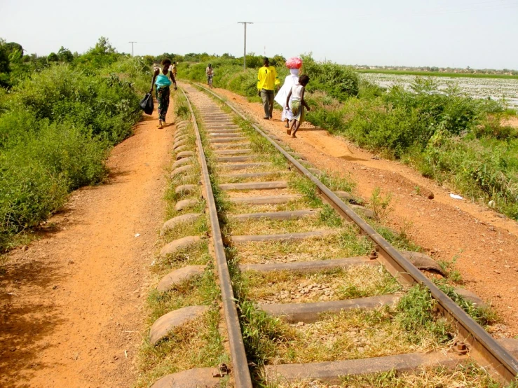 some people walking near the train tracks while other people walk away