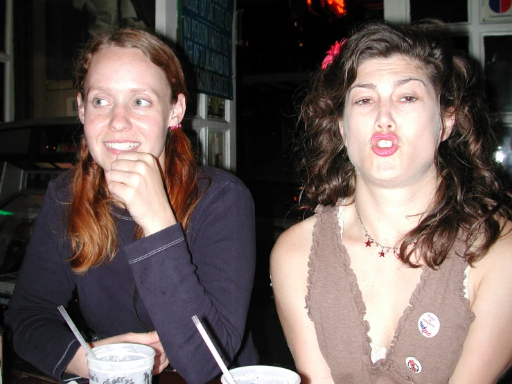 two women sitting at a table with drinks and one holding her face to her mouth