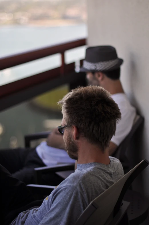 two men sitting down in a chair by the water