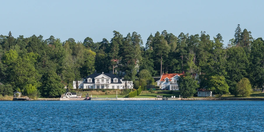 a boat floats near a white, old home on a lake