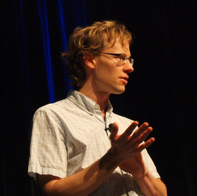 a man wearing glasses while making a speech