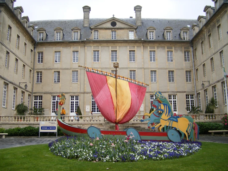 a sculpture of a ship in a flower bed in front of a building