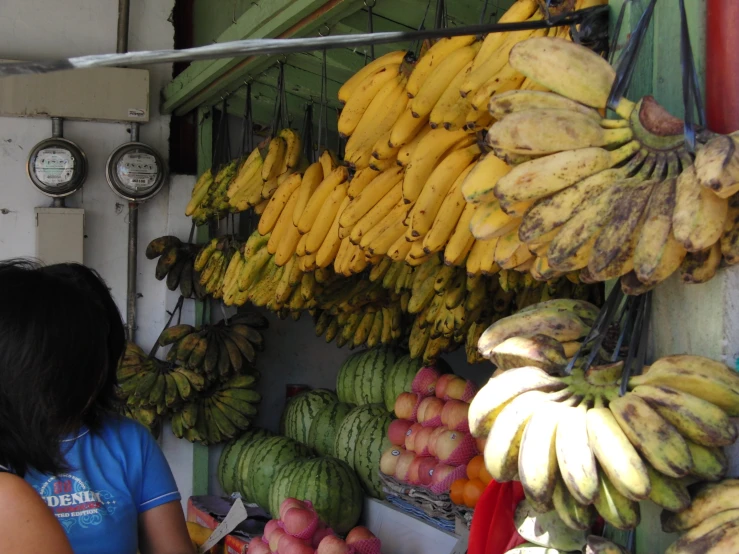 a woman buying some bananas in front of a fruit stand