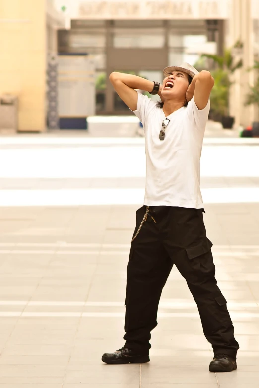 man in a white shirt, black pants and tennis shoes looking up to his hat