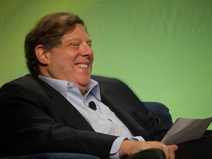 a man in a suit smiles while holding a piece of paper