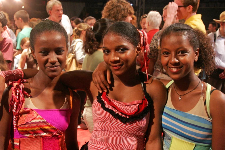 three girls in dresses stand beside each other in a crowd
