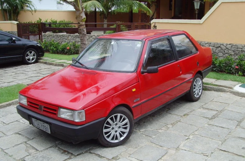 a red hatchback parked on the sidewalk with other cars