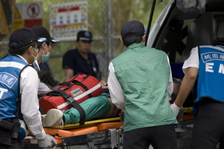 a group of medical personnel are surrounding the man lying on an ambulance