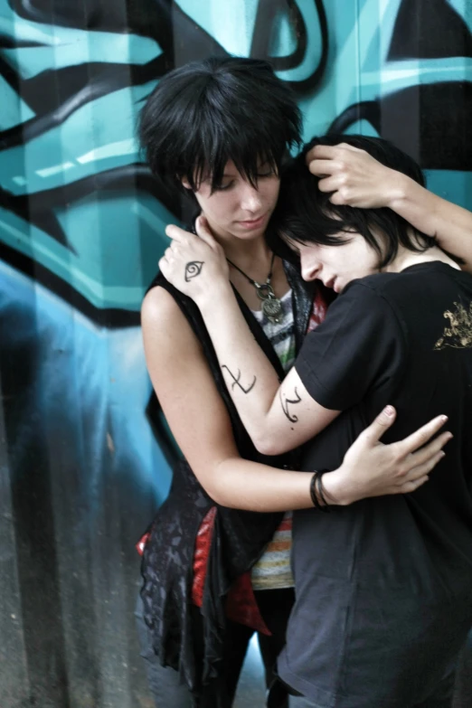 two people standing side by side in front of a wall with graffiti