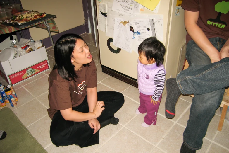 a woman and her child are sitting near a refrigerator