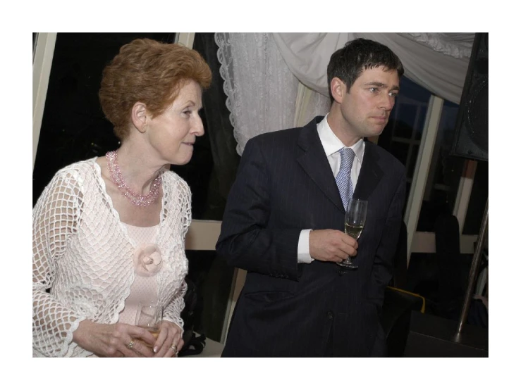 a lady standing next to a man and holding a glass