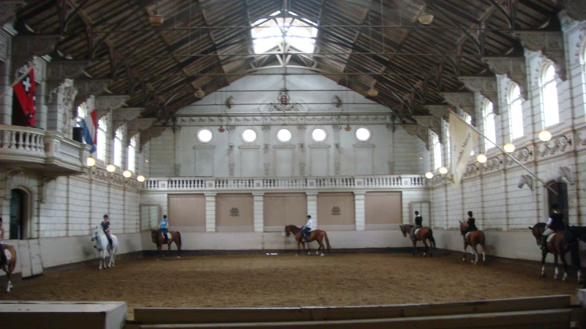 several horseback riders, riding on the backs of horses inside of a building