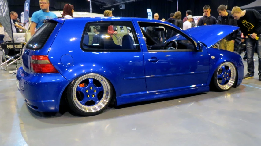 a blue car with an open hood is parked at the show