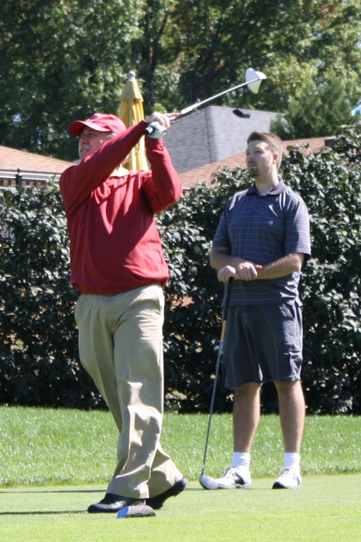 a man swinging a golf club with another person watching him