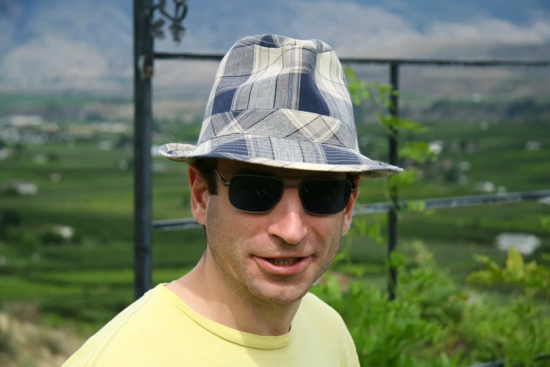 a man in a plaid hat and sunglasses smiles
