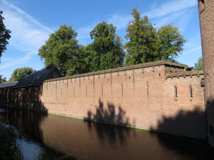 a brown brick wall by the water has trees in the background