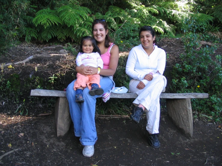 two ladies sitting on a bench with their baby