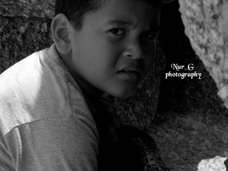 an asian boy standing on the rocks near a large rock