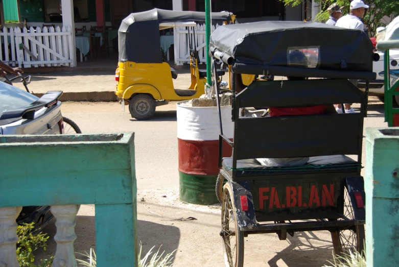 an old small cart parked next to a building with people standing around