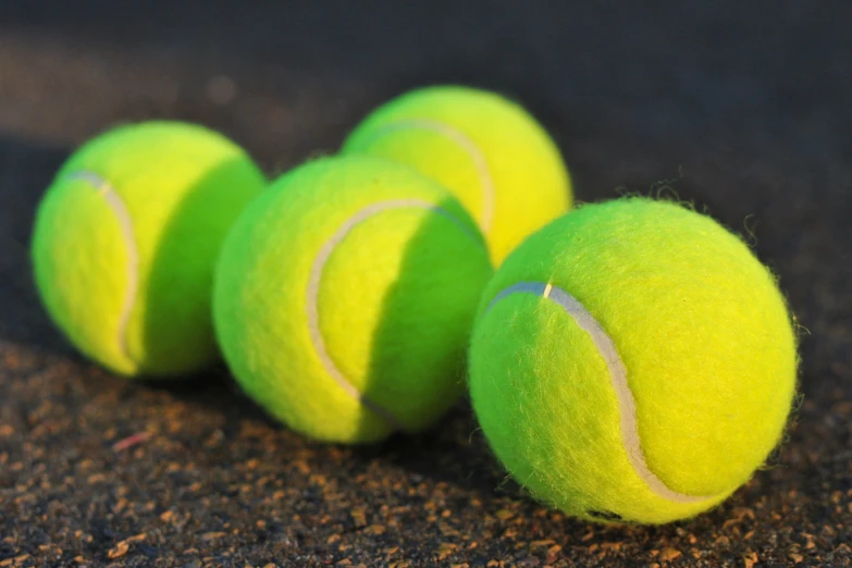 four green tennis balls on a brown surface