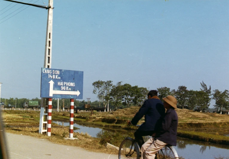 a man on a bike rides beside a man that is wearing a hat