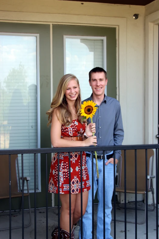 the two people are holding a sunflower outside