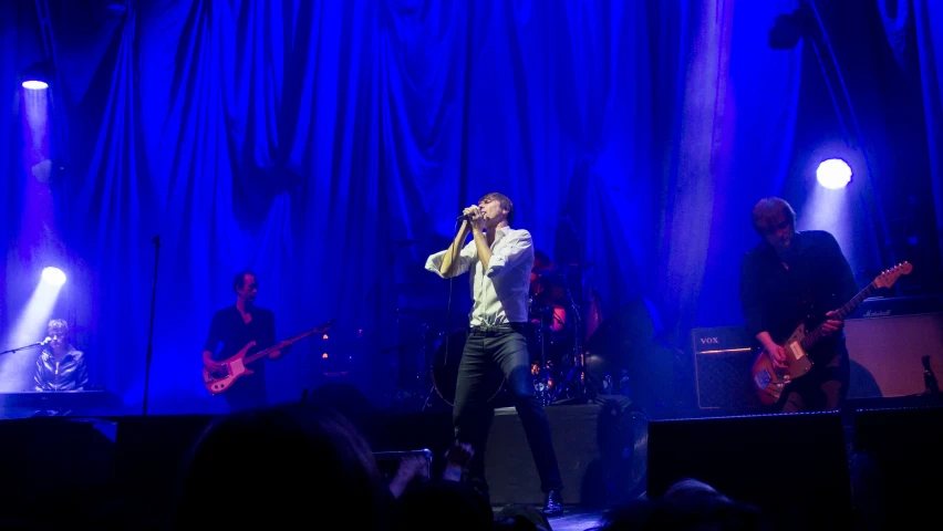 man holding a microphone in front of blue lights and playing guitar