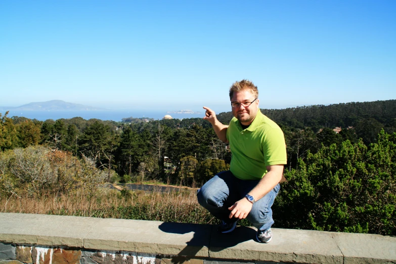 a man crouching on the edge of a wall pointing at soing