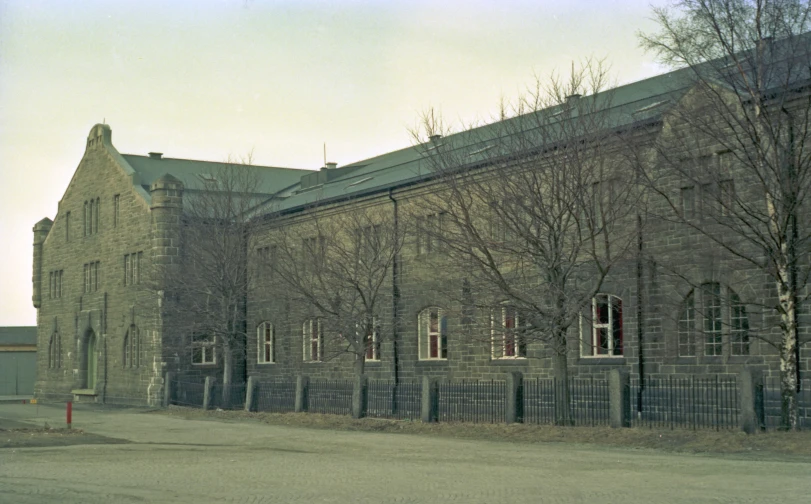 old grey brick building with trees near road