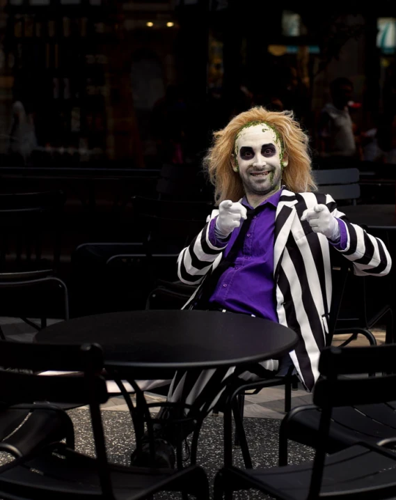 a creepy clown wearing a striped jacket sits at a table