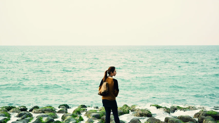 a girl is standing on rocks next to the water