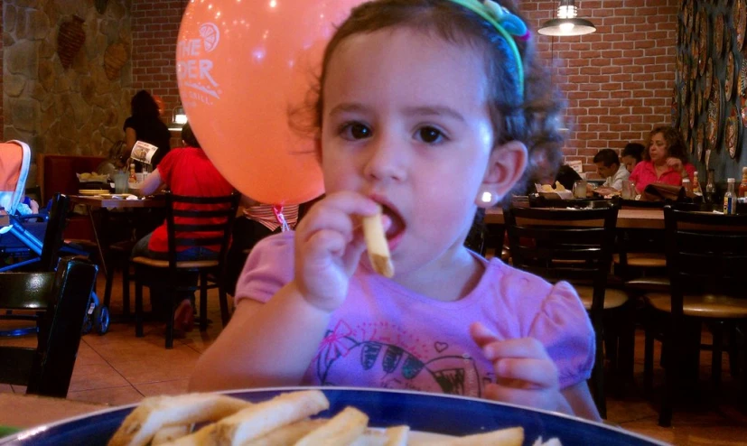 the little girl is enjoying her french fries with her party hat on