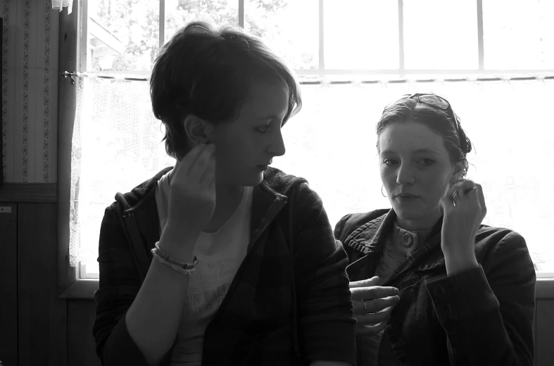 two women look at their phones while sitting on a chair