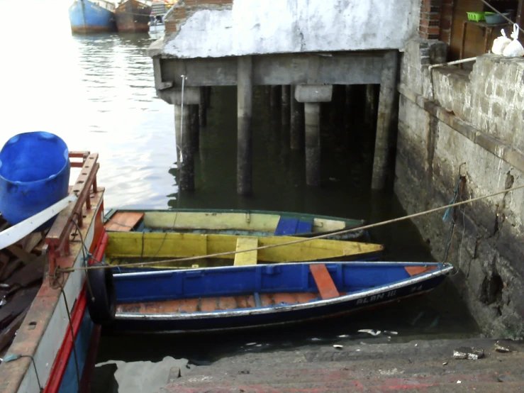 a blue and yellow boat is next to a building with water and dock in background