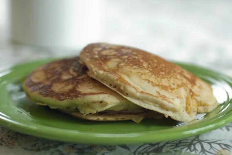 two pancakes on a green plate with a white cup