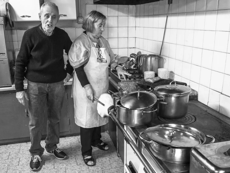 a man and a woman standing in front of pots on the stove