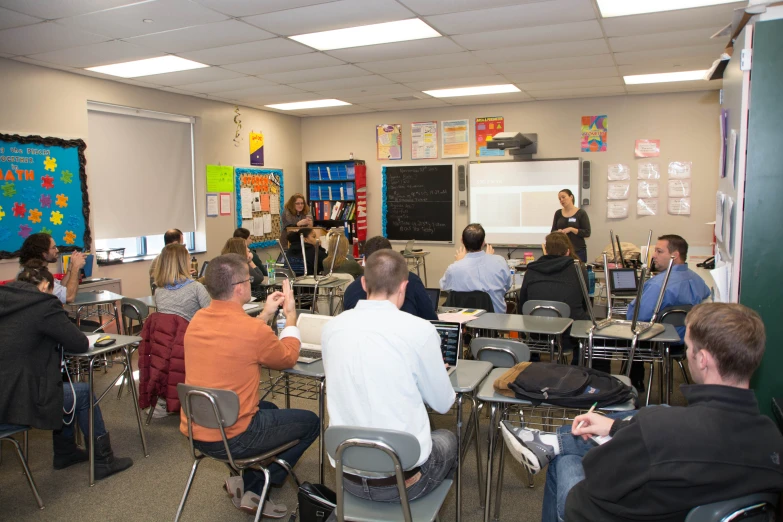 a classroom full of people sitting and standing in front of a chalk board