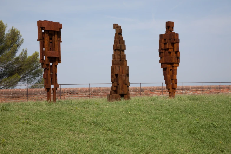 three very tall rusty sculptures stand in the grass