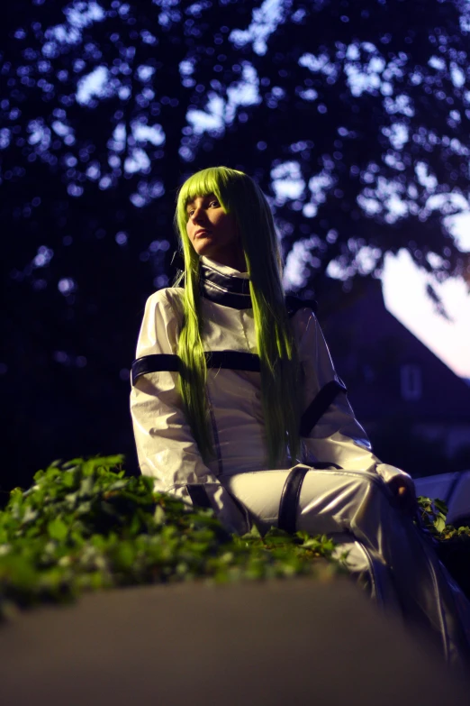 a woman with green hair is sitting down in front of trees