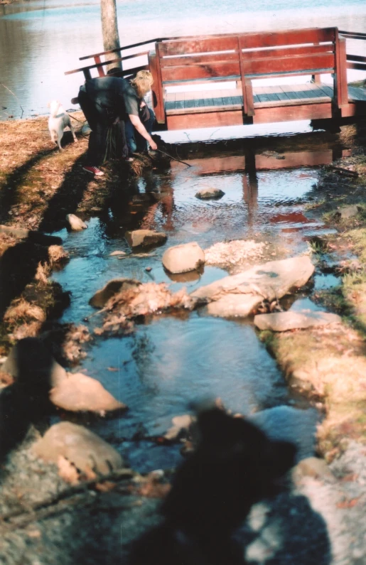 a man standing on the side of a small river next to a bench