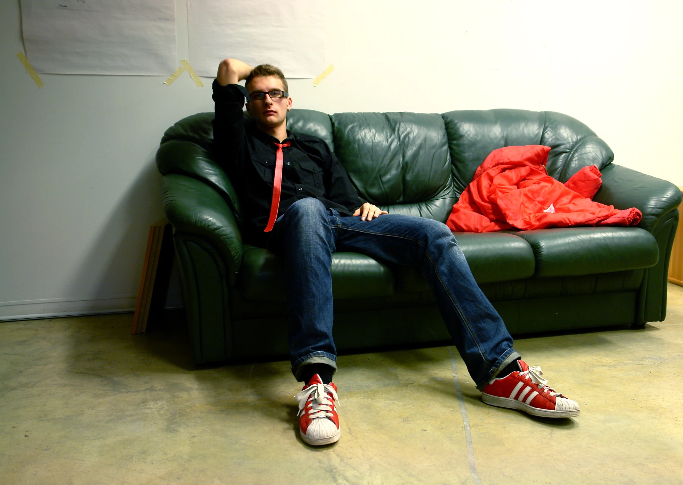 a man in black jacket and jeans sitting on a black leather couch