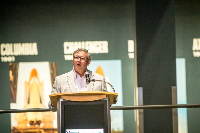 a man with glasses speaking on stage at a conference