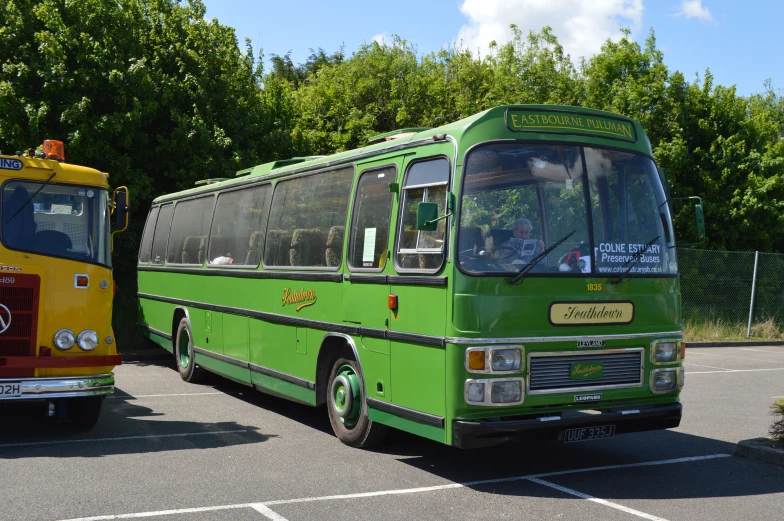 an older green bus parked next to a yellow and red bus