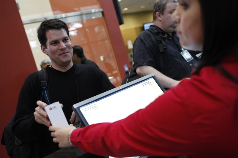 a man holding up his laptop while standing next to a woman