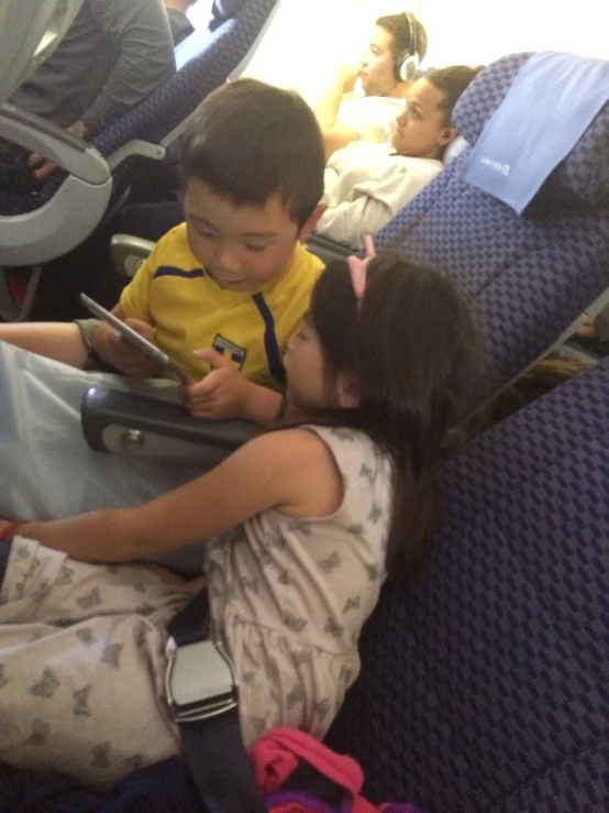 a little boy and girl sitting on an airplane seat next to each other