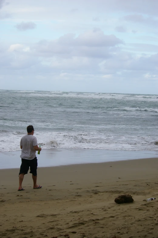 man standing on beach holding two items next to ocean