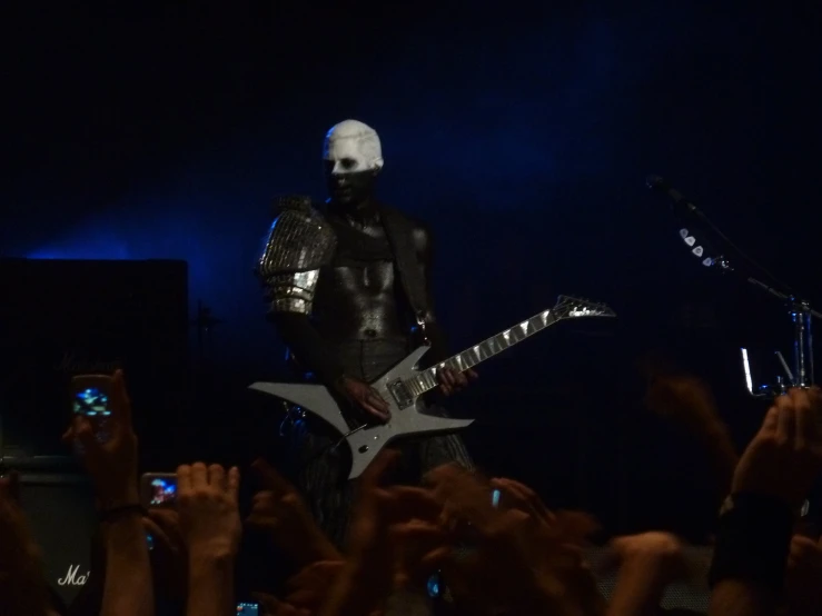 a man in a black costume plays guitar on stage with his hands in the air