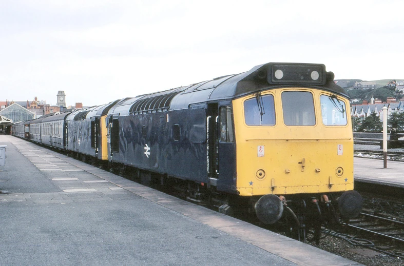 a yellow and blue train passing by a loading platform