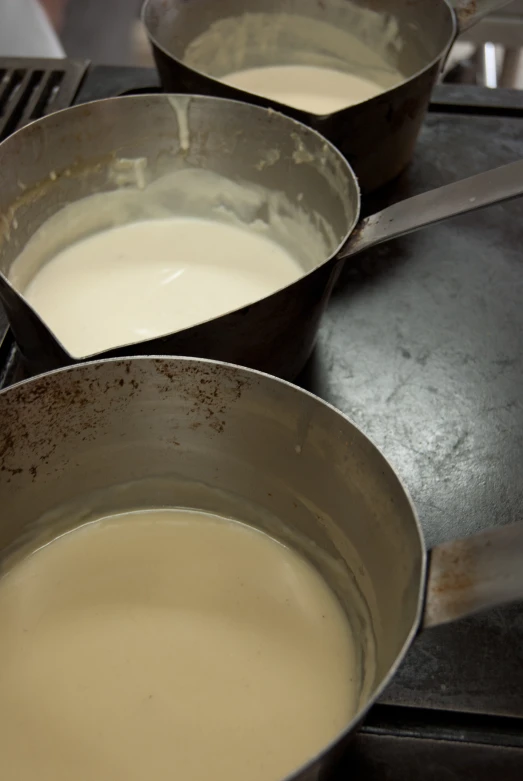 three pans on top of a stove holding different kind of sauce