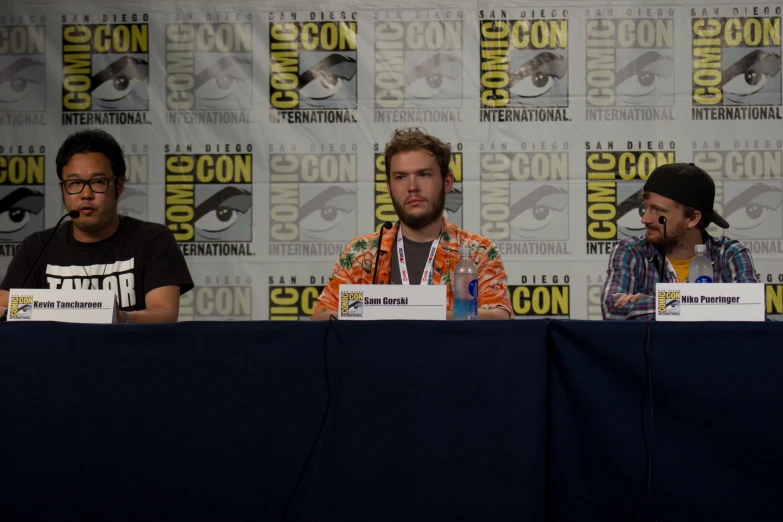 the men are sitting at the table during a comic convention